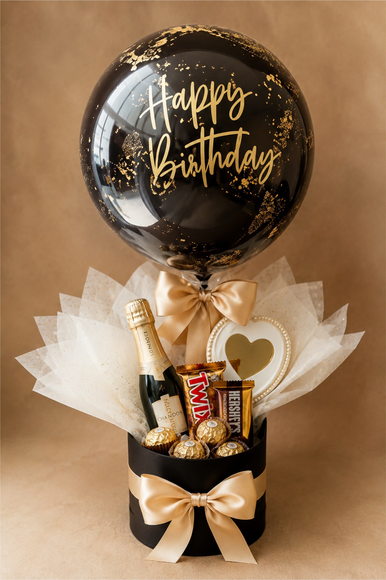 A black and gold Happy Birthday balloon arrangement over a gift box with champagne and chocolates.